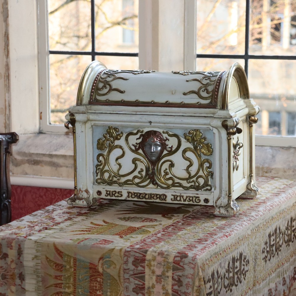 A cream-painted domed Art Nouveau casket featuring gilt metal whiplash scrollwork, a central relief mask, and a Latin inscription around the base. View IV