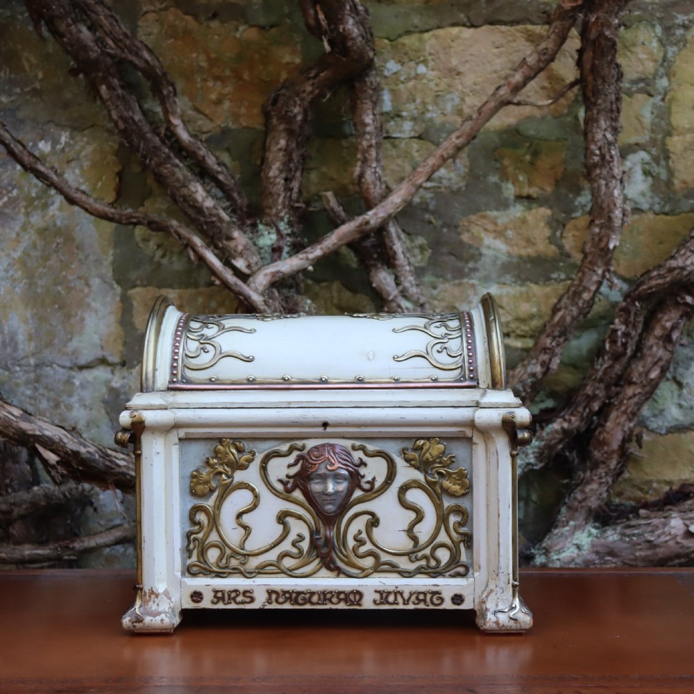 A cream-painted domed Art Nouveau casket featuring gilt metal whiplash scrollwork, a central relief mask, and a Latin inscription around the base. View V