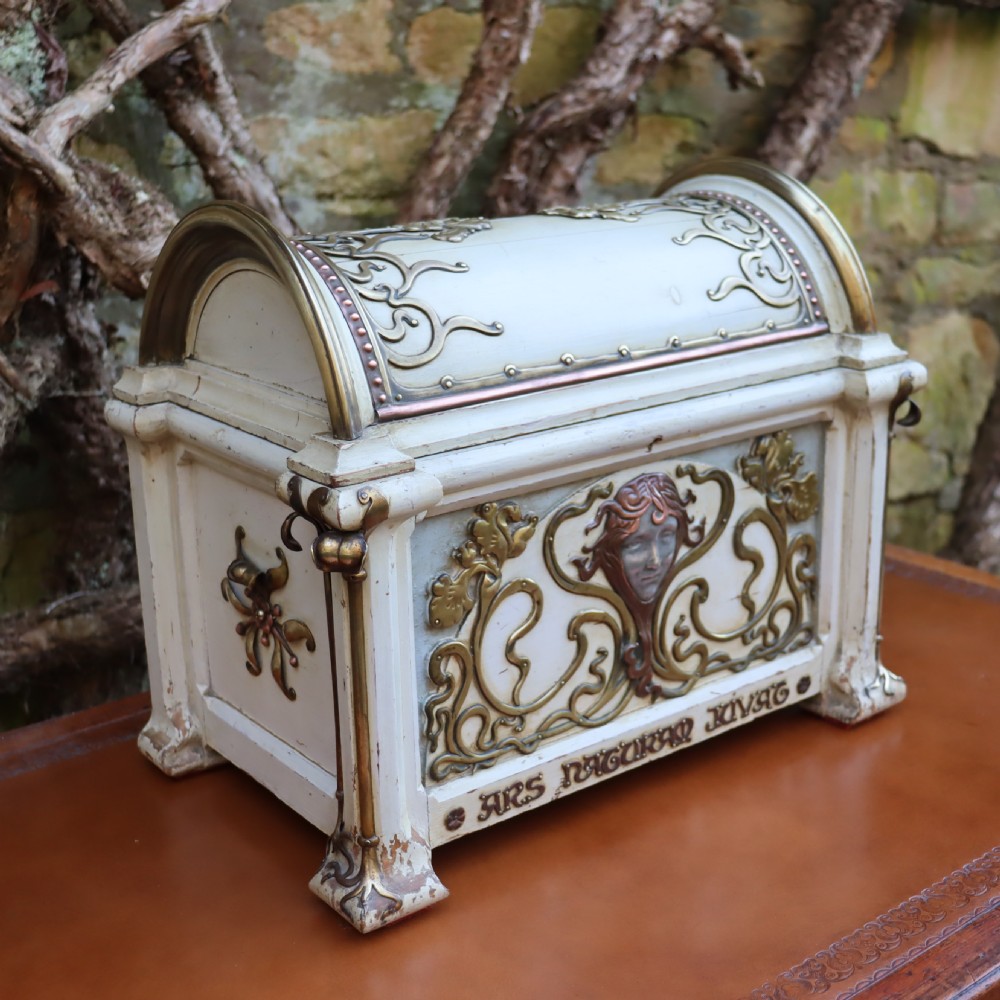 A cream-painted domed Art Nouveau casket featuring gilt metal whiplash scrollwork, a central relief mask, and a Latin inscription around the base. View VI