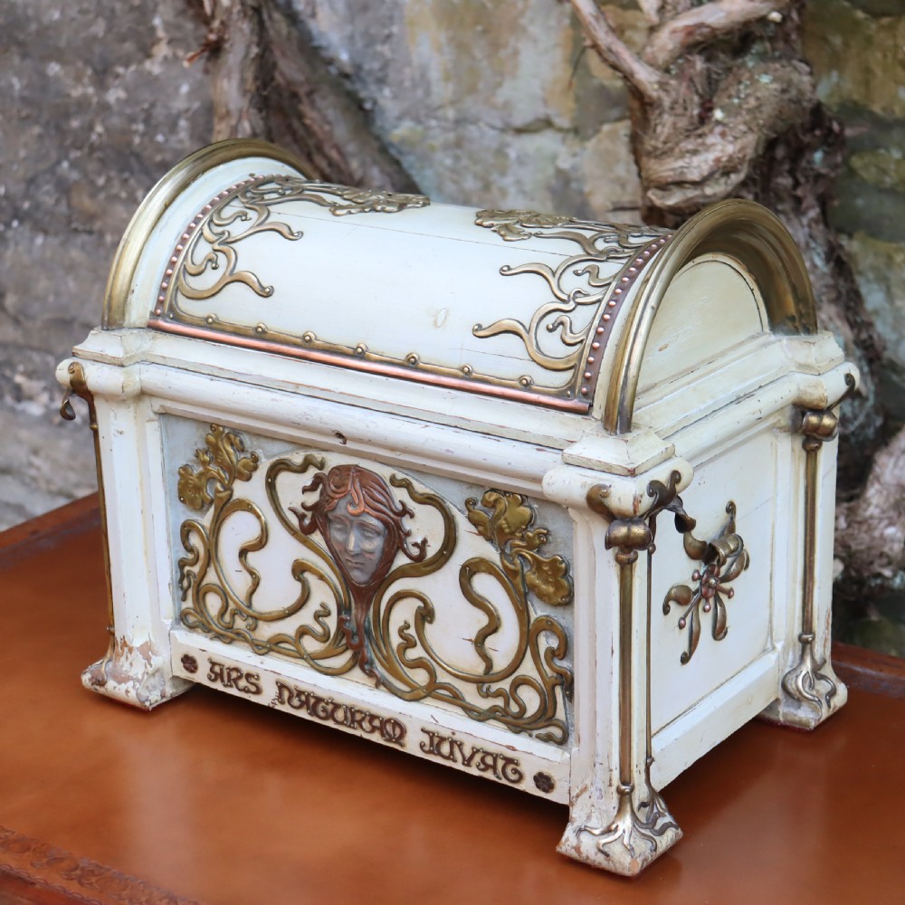 A cream-painted domed Art Nouveau casket featuring gilt metal whiplash scrollwork, a central relief mask, and a Latin inscription around the base. View VII