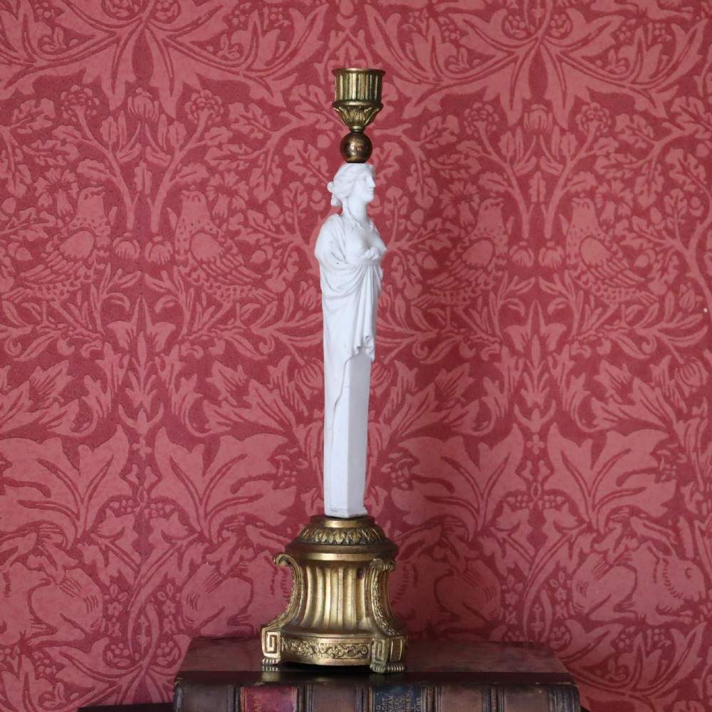A 19th-century Neoclassical candlestick featuring a chased gilded bronze base and socket holding a sculpted white biscuit porcelain caryatid figure.