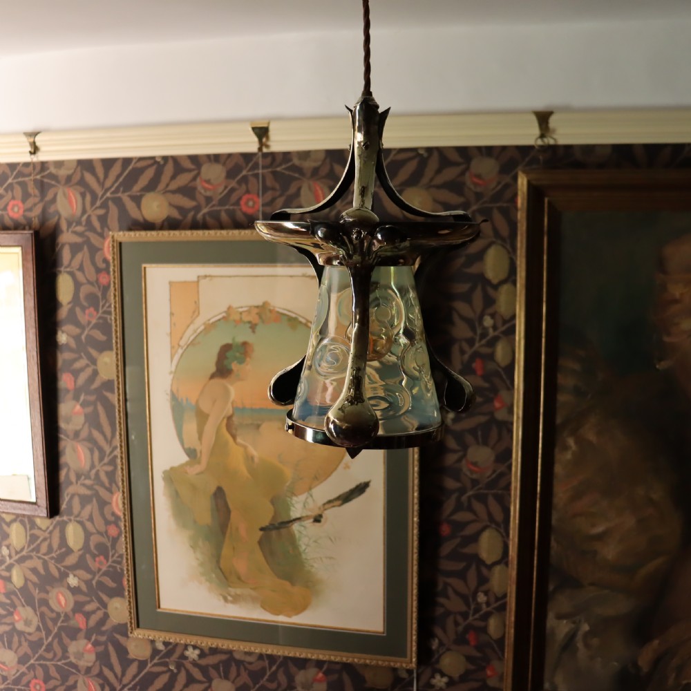 An Arts and Crafts brass ceiling light with organic botanical straps holding a white opalescent glass shade. View III