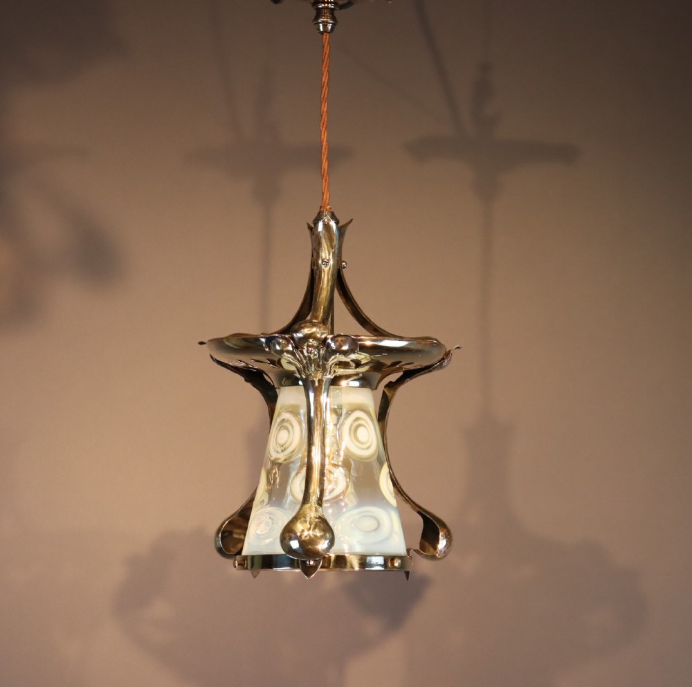 An Arts and Crafts brass ceiling light with organic botanical straps holding a white opalescent glass shade. View II