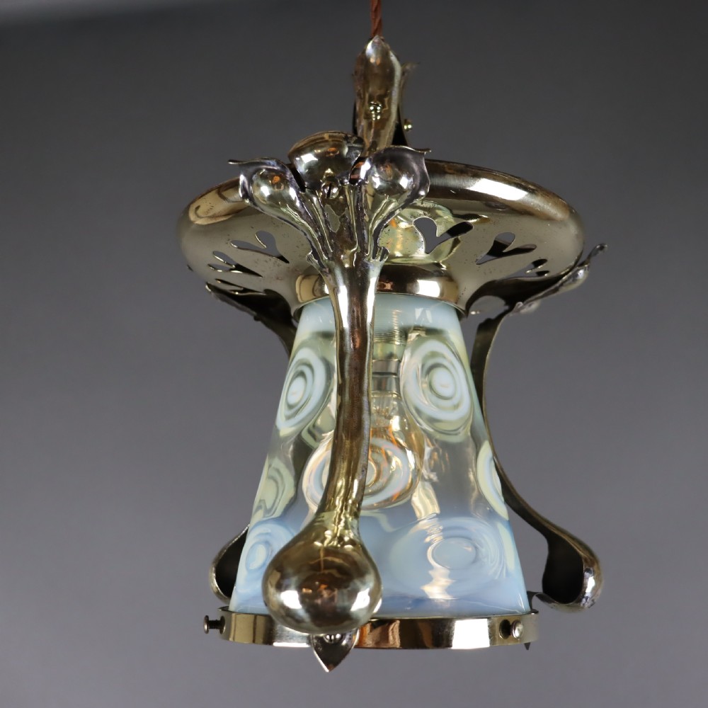 An Arts and Crafts brass ceiling light with organic botanical straps holding a white opalescent glass shade. View IV