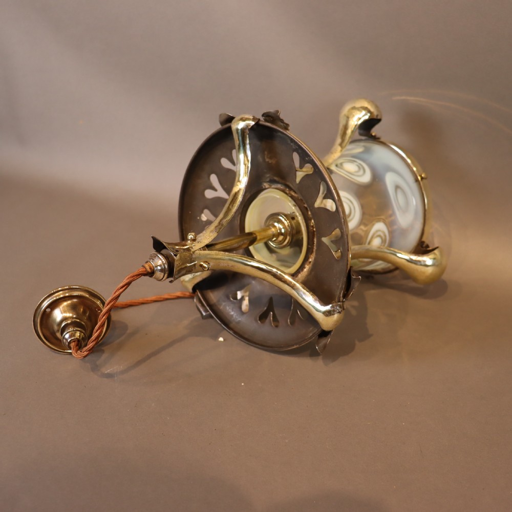 An Arts and Crafts brass ceiling light with organic botanical straps holding a white opalescent glass shade. View VI