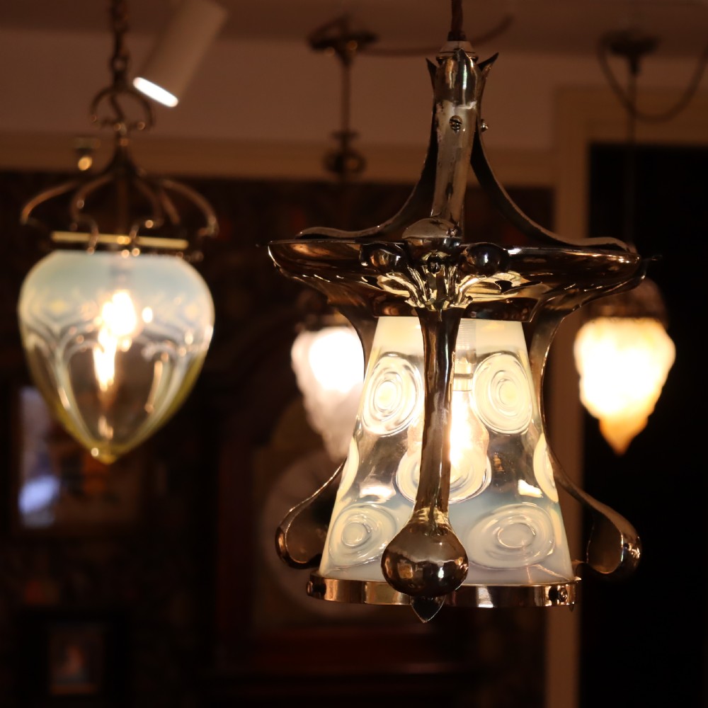 An Arts and Crafts brass ceiling light with organic botanical straps holding a white opalescent glass shade. View VII