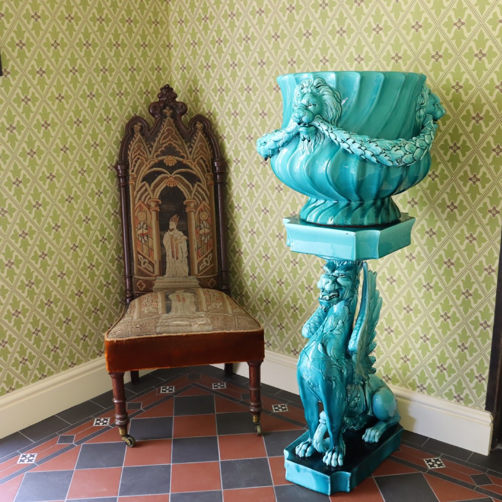A bright turquoise glazed ceramic jardiniere with lion head swags resting on a matching winged griffin pedestal stand. View X