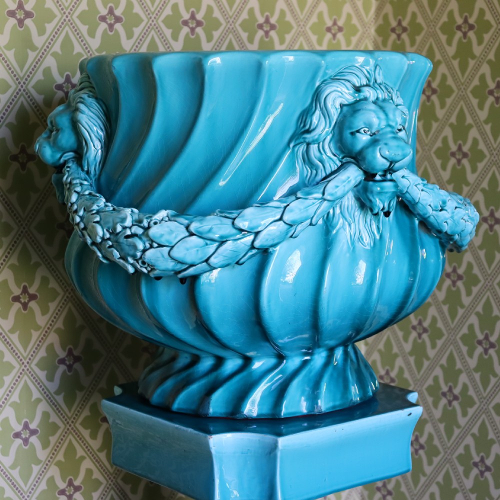 A bright turquoise glazed ceramic jardiniere with lion head swags resting on a matching winged griffin pedestal stand. View VI