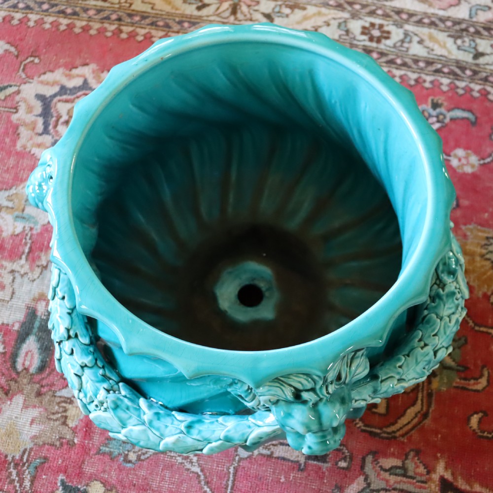 A bright turquoise glazed ceramic jardiniere with lion head swags resting on a matching winged griffin pedestal stand. View VII