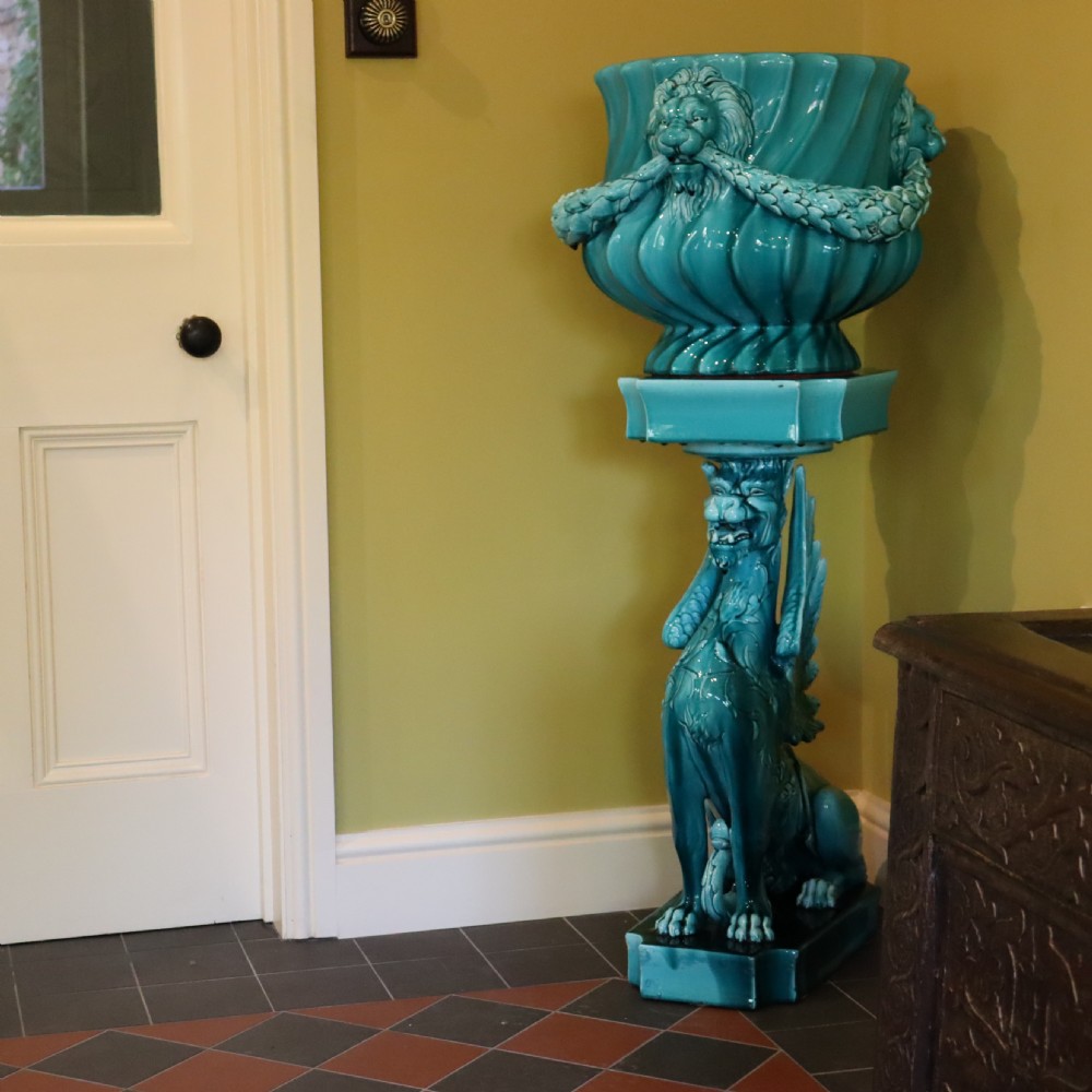 A bright turquoise glazed ceramic jardiniere with lion head swags resting on a matching winged griffin pedestal stand. View II