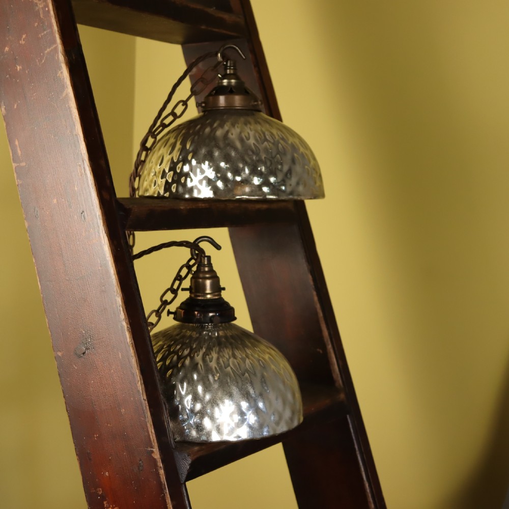 A pair of circa 1920 mercury glass pendant lights featuring textured silvered shades and dark brass galleries with hanging hooks. View V