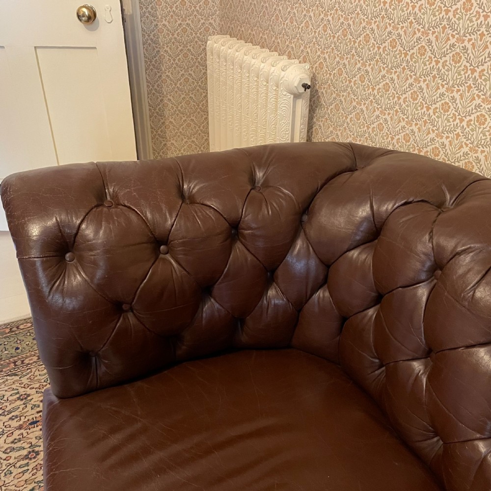 A three-seater brown leather Chesterfield sofa featuring deep button tufting, scrolled arms, and turned wooden legs with castors. View II