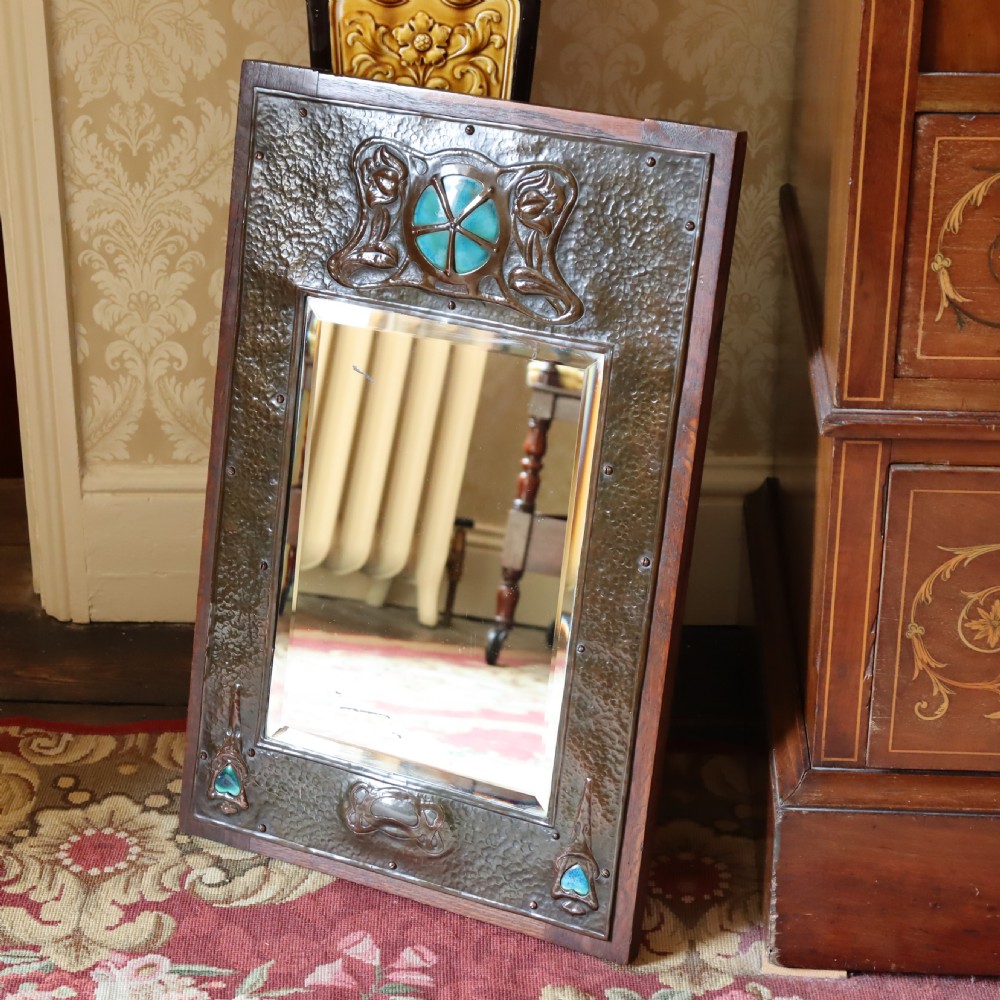 An Arts and Crafts repoussé and oak framed mirror.