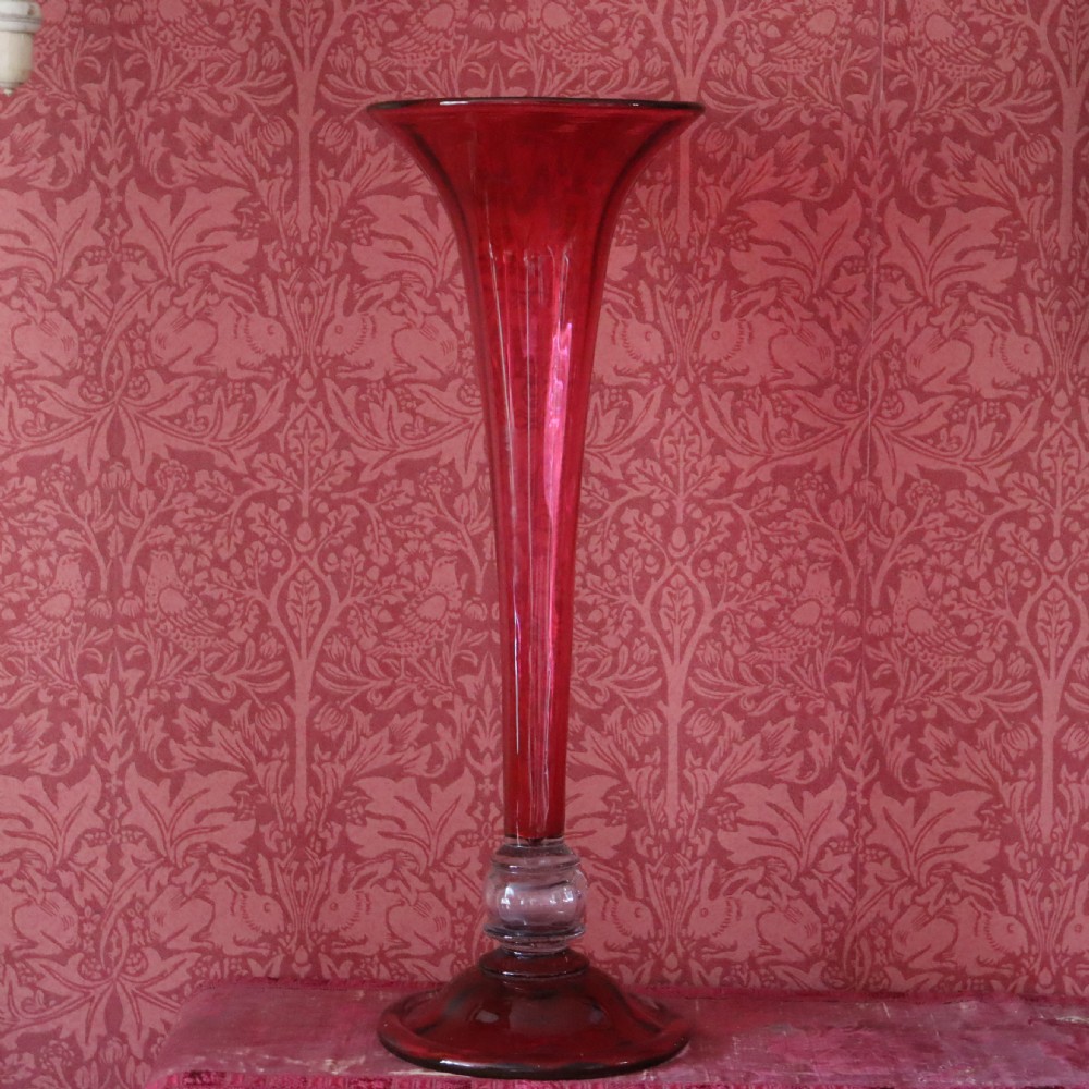 A tall Victorian trumpet-shaped vase made of deep red cranberry glass with a clear glass knop and circular foot.