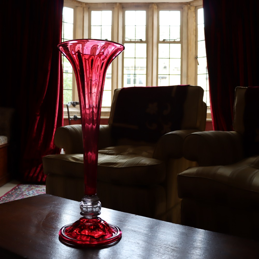 A tall Victorian trumpet-shaped vase made of deep red cranberry glass with a clear glass knop and circular foot. View VI