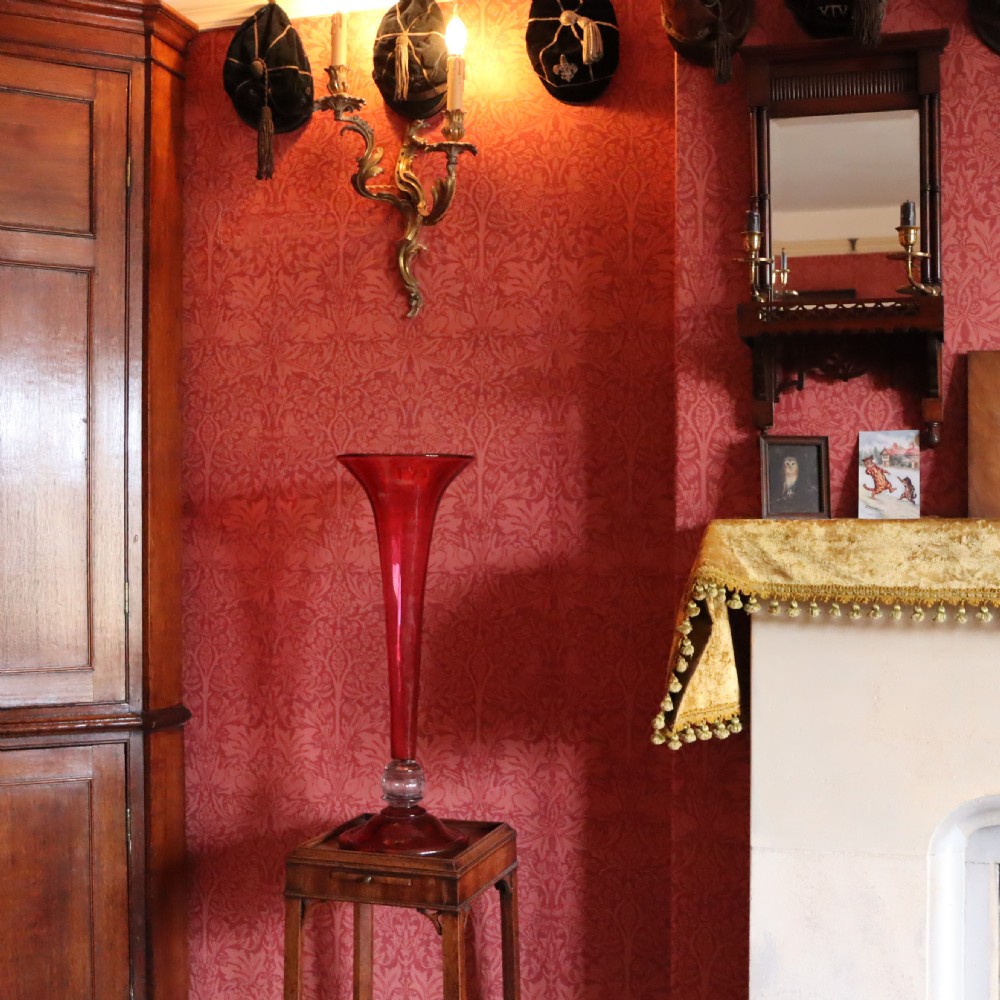 A tall Victorian trumpet-shaped vase made of deep red cranberry glass with a clear glass knop and circular foot. View VII