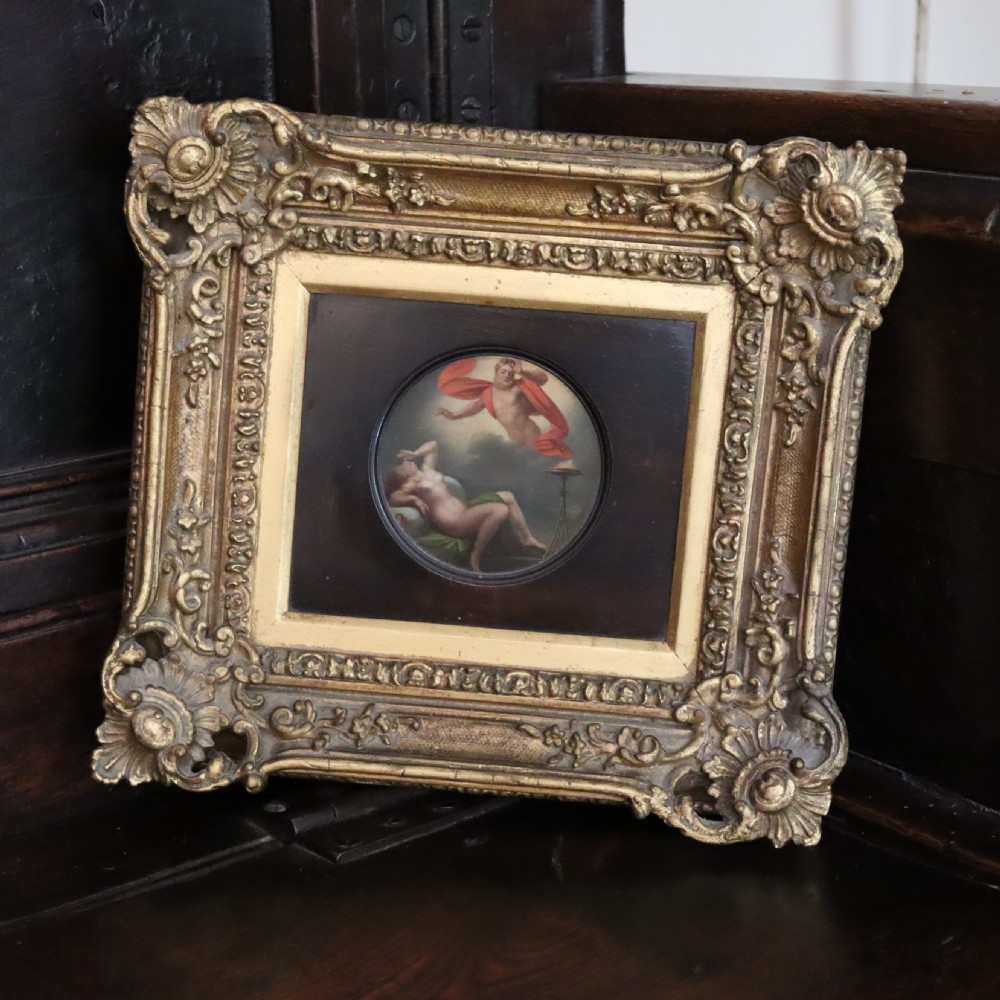 A small circular early 19th-century mythological oil painting depicting a reclining nude nymph and floating male god, encased in a square, highly ornate giltwood frame. View V