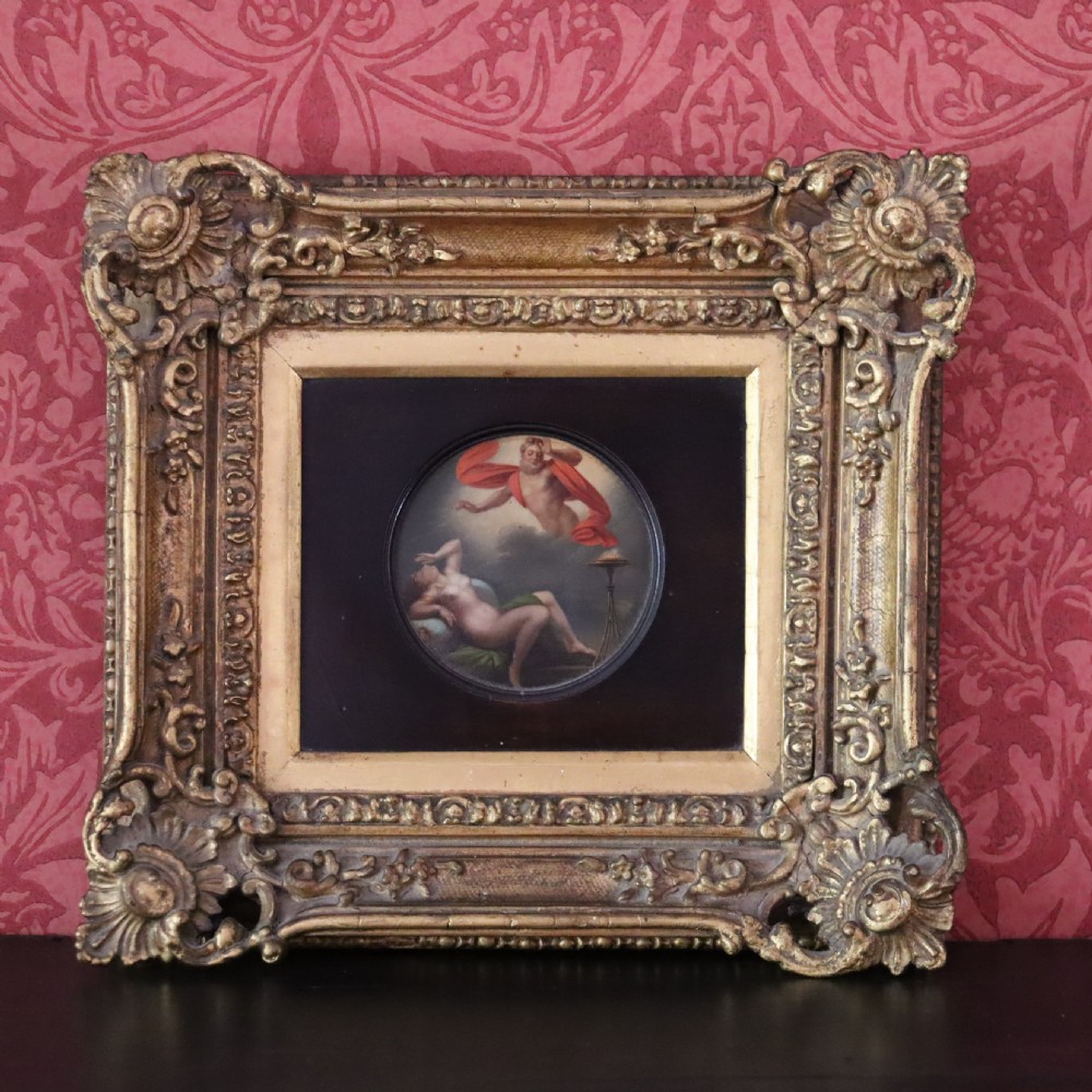 A small circular early 19th-century mythological oil painting depicting a reclining nude nymph and floating male god, encased in a square, highly ornate giltwood frame. View IX