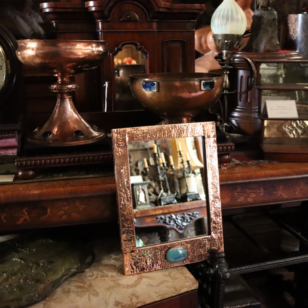 A rectangular hand-hammered copper wall mirror featuring a single blue-green ceramic cabochon mounted at the bottom centre frame. View II
