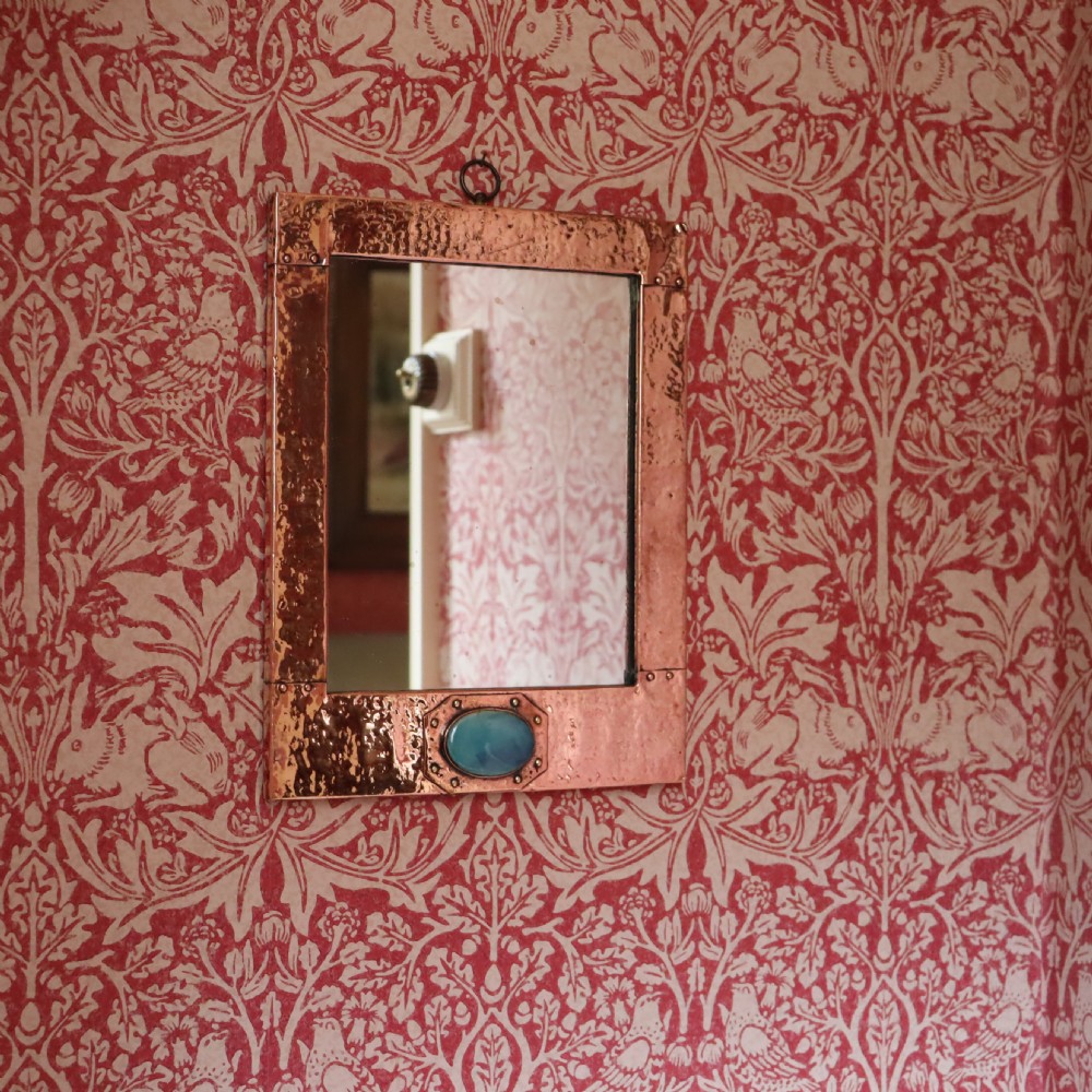 A rectangular hand-hammered copper wall mirror featuring a single blue-green ceramic cabochon mounted at the bottom centre frame. View III