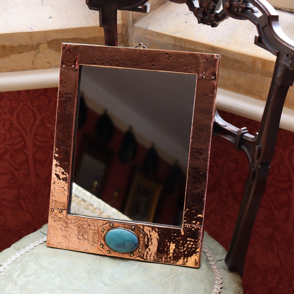A rectangular hand-hammered copper wall mirror featuring a single blue-green ceramic cabochon mounted at the bottom centre frame. View IV
