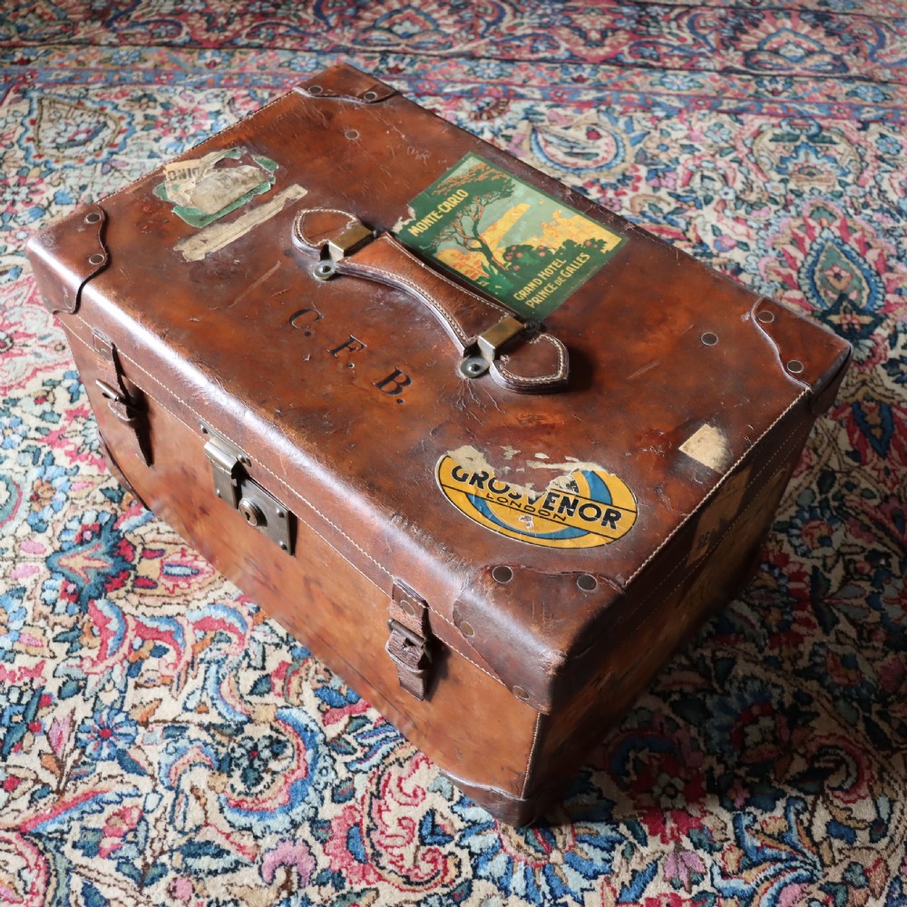 An Edwardian warm brown leather travel trunk with brass locks, leather straps, stencilled monogram initials, and vintage hotel labels. View II