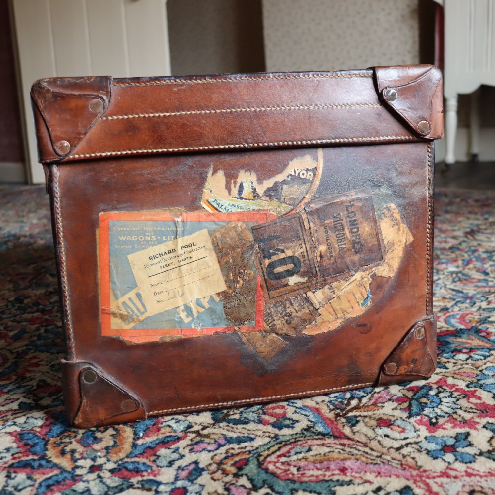 An Edwardian warm brown leather travel trunk with brass locks, leather straps, stencilled monogram initials, and vintage hotel labels. View III