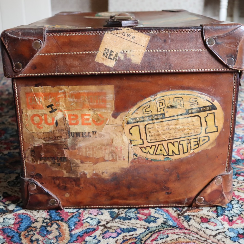 An Edwardian warm brown leather travel trunk with brass locks, leather straps, stencilled monogram initials, and vintage hotel labels. View V