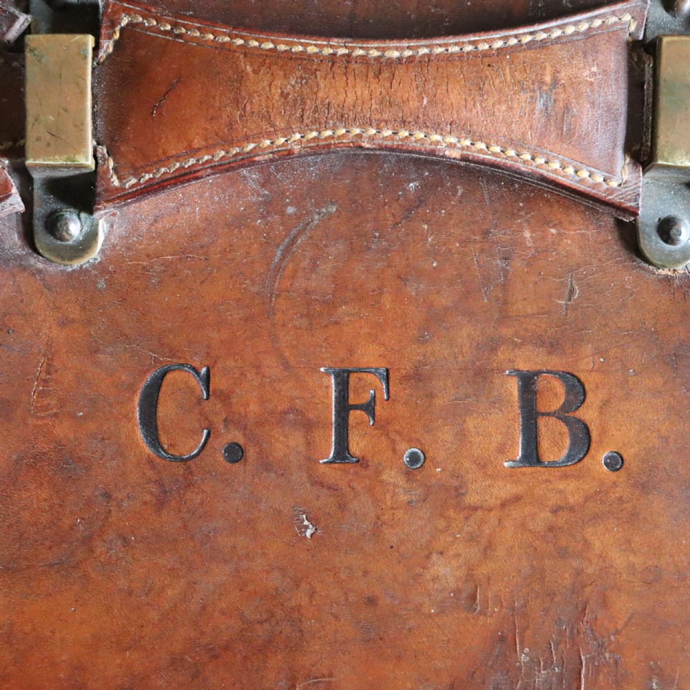 An Edwardian warm brown leather travel trunk with brass locks, leather straps, stencilled monogram initials, and vintage hotel labels. View VII