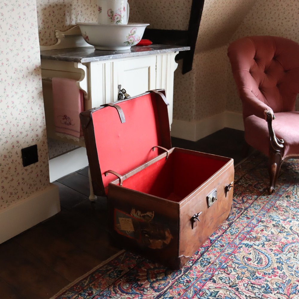 An Edwardian warm brown leather travel trunk with brass locks, leather straps, stencilled monogram initials, and vintage hotel labels. View VIII