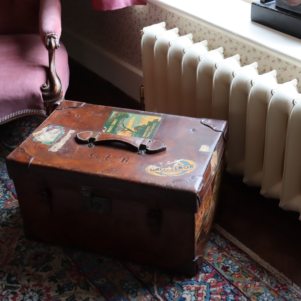 An Edwardian warm brown leather travel trunk with brass locks, leather straps, stencilled monogram initials, and vintage hotel labels. View IX
