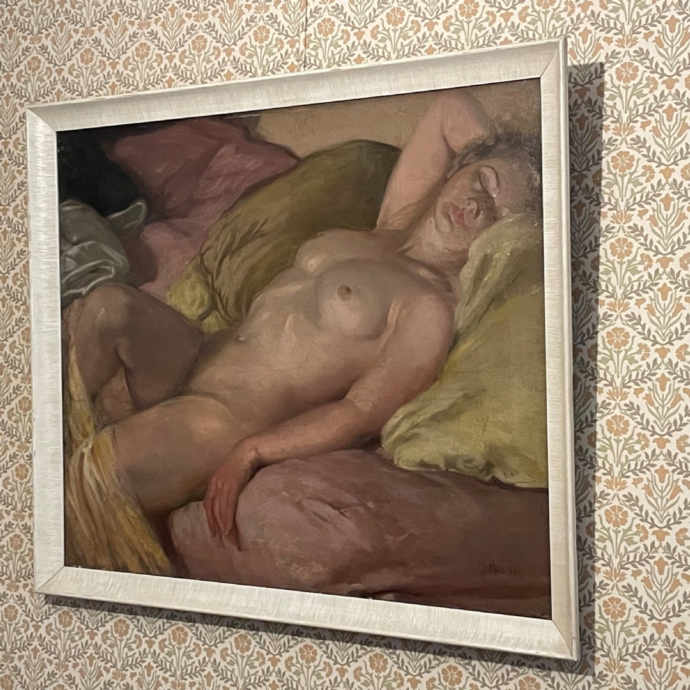 A framed oil painting on canvas depicting a reclining female figure resting on muted pink and olive yellow cushions.