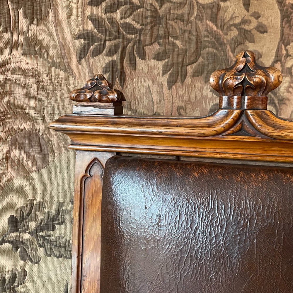 A pair of Victorian Gothic Revival oak hall chairs featuring carved cresting, leather upholstered back panels, solid oak seats, and rectangular stretchers. View III