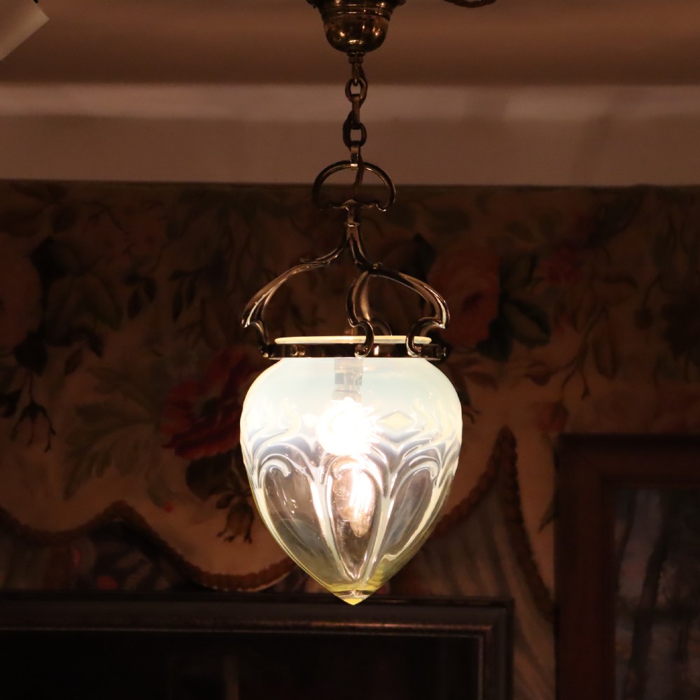 An Arts and Crafts brass pendant light featuring a hanging chain, curved brass frame, and a bulbous opalescent glass shade with molded relief patterns.