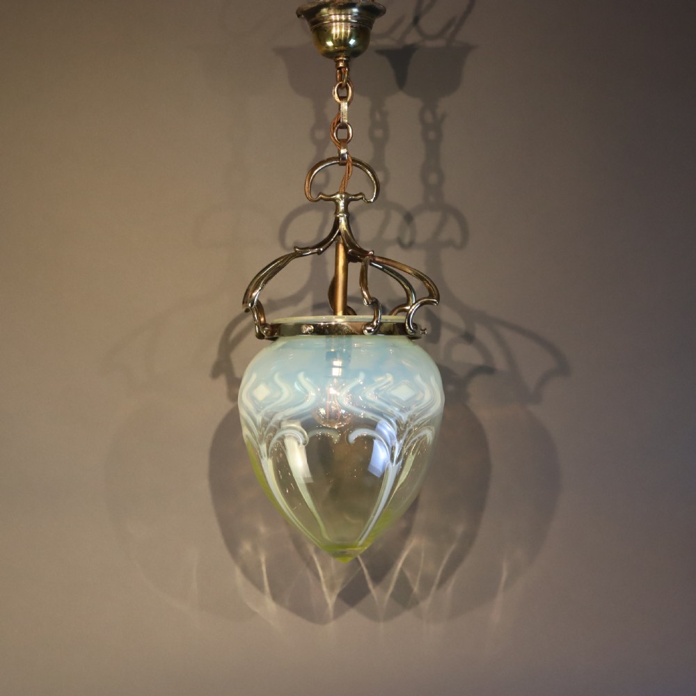 An Arts and Crafts brass pendant light featuring a hanging chain, curved brass frame, and a bulbous opalescent glass shade with molded relief patterns. View II