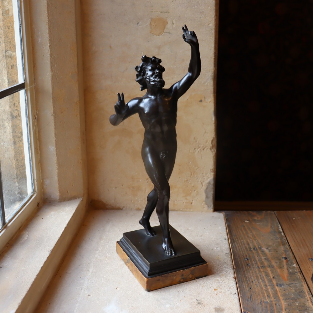 A dark patinated bronze figure depicting the Dancing Faun of Pompeii mounted on a moulded bronze and marble plinth base.