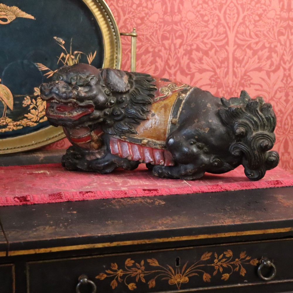 A hand-carved wooden Chinese foo dog sculpture featuring polychrome painted details in red, yellow, and dark green. View II