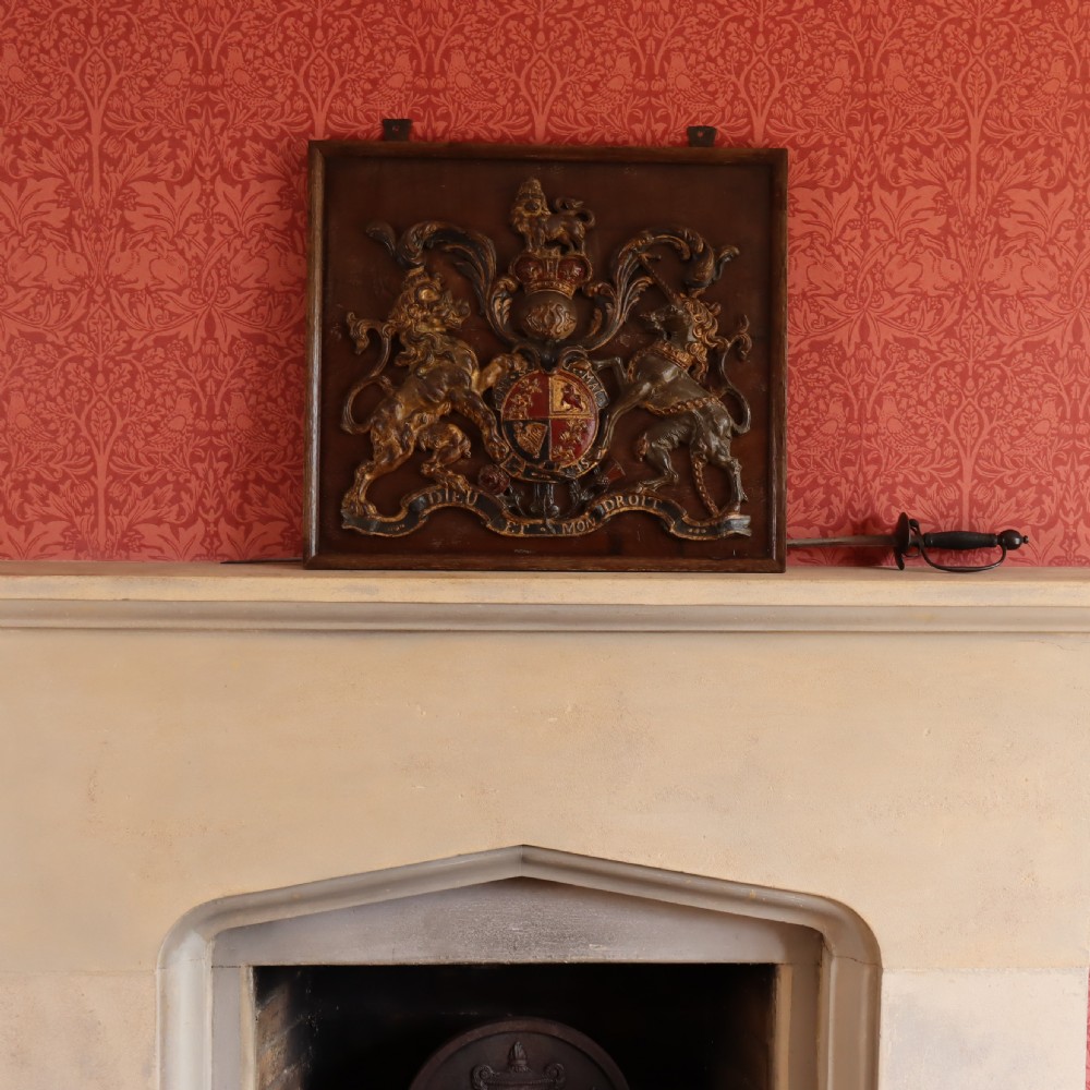 A square dark wood panel featuring a central relief of the British Royal coat of arms with gilded details and metal hanging fixtures at the top. View VIII