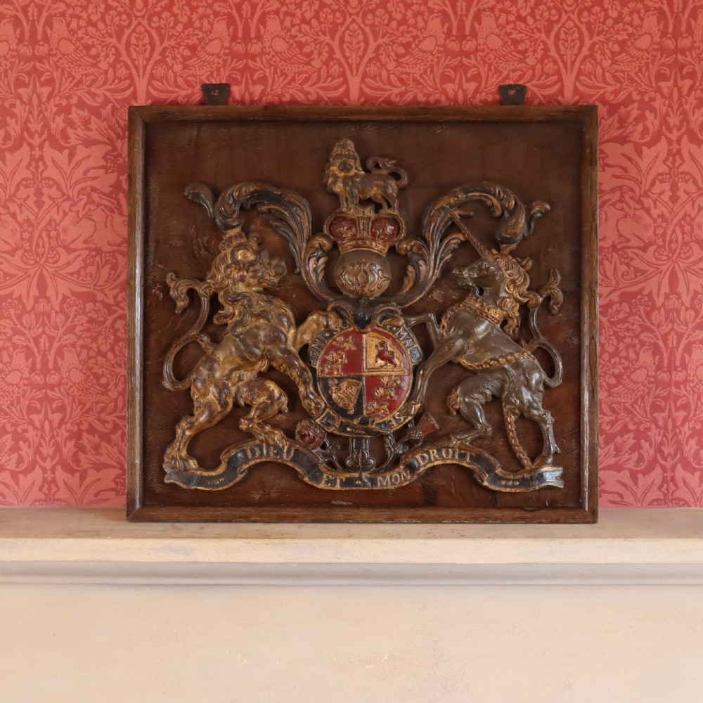 A square dark wood panel featuring a central relief of the British Royal coat of arms with gilded details and metal hanging fixtures at the top. View II