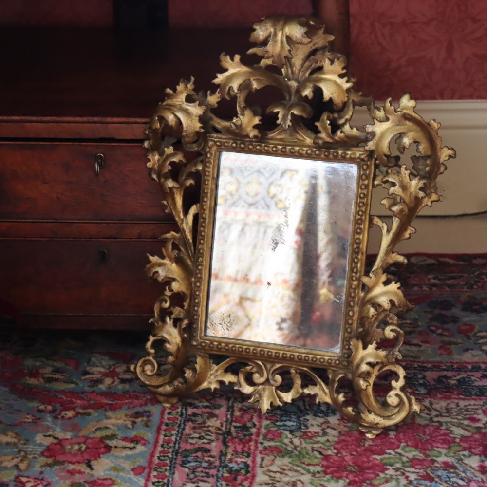 An antique Florentine wall mirror featuring a carved giltwood frame decorated with scrolling acanthus leaves and a beaded inner border surrounding an aged glass plate.