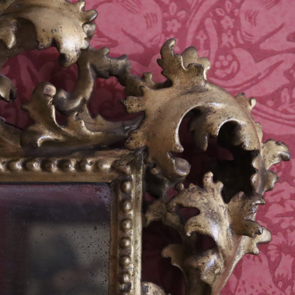 An antique Florentine wall mirror featuring a carved giltwood frame decorated with scrolling acanthus leaves and a beaded inner border surrounding an aged glass plate. View IV