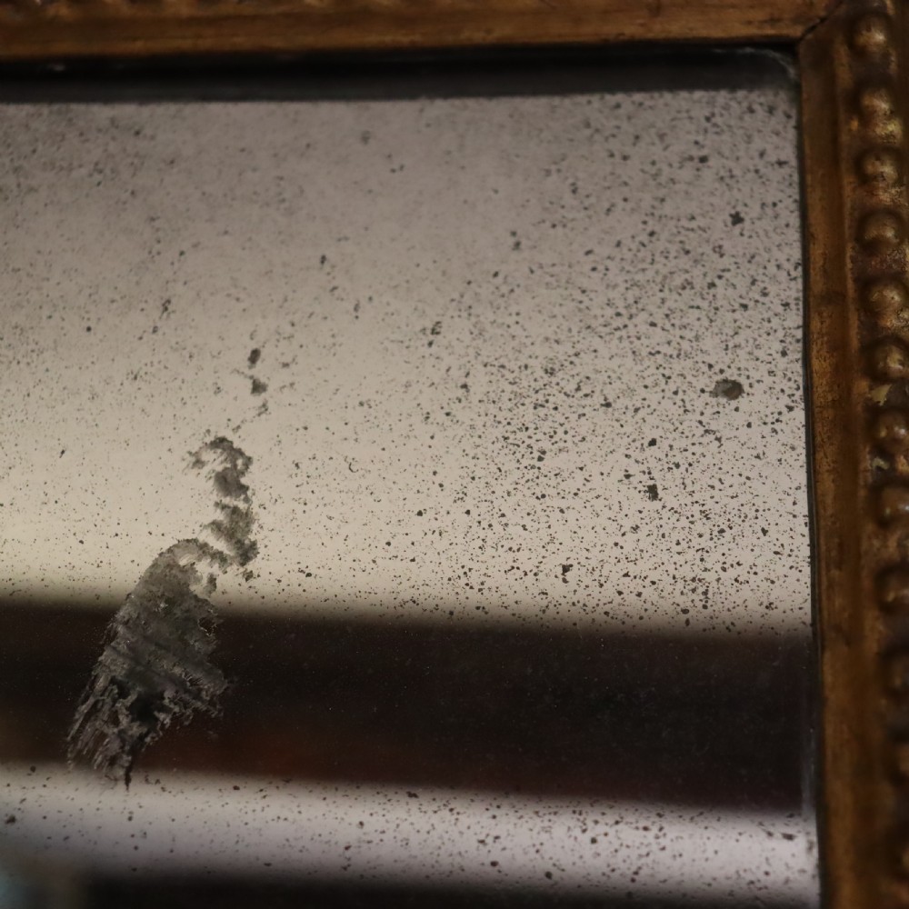 An antique Florentine wall mirror featuring a carved giltwood frame decorated with scrolling acanthus leaves and a beaded inner border surrounding an aged glass plate. View V
