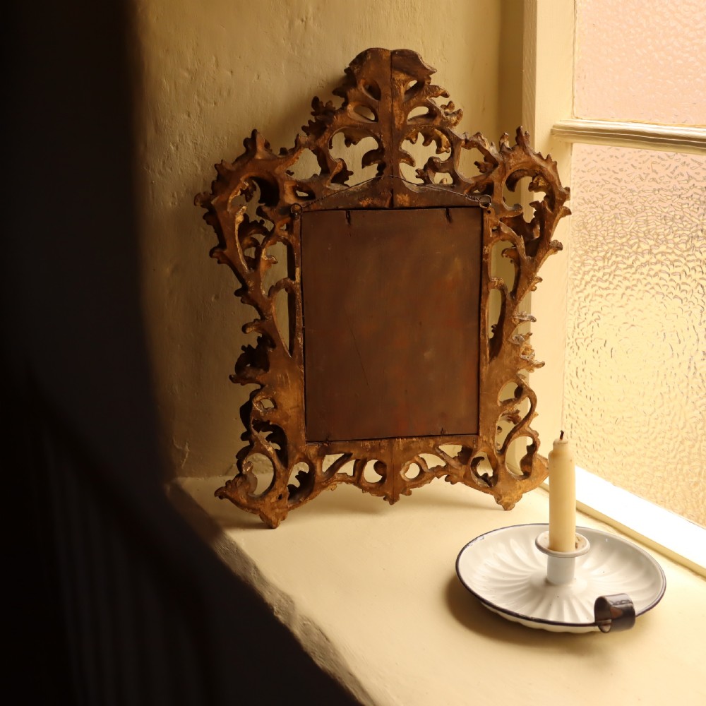 An antique Florentine wall mirror featuring a carved giltwood frame decorated with scrolling acanthus leaves and a beaded inner border surrounding an aged glass plate. View VI