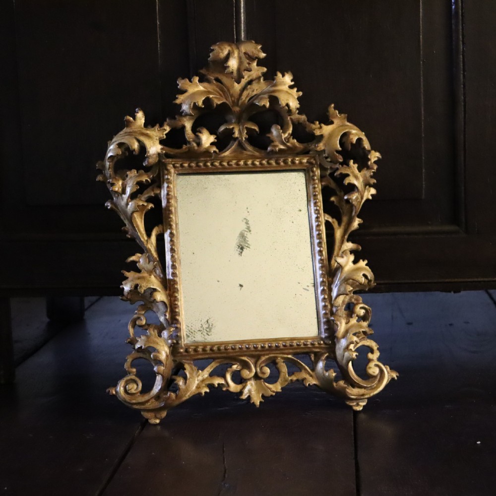 An antique Florentine wall mirror featuring a carved giltwood frame decorated with scrolling acanthus leaves and a beaded inner border surrounding an aged glass plate. View VII