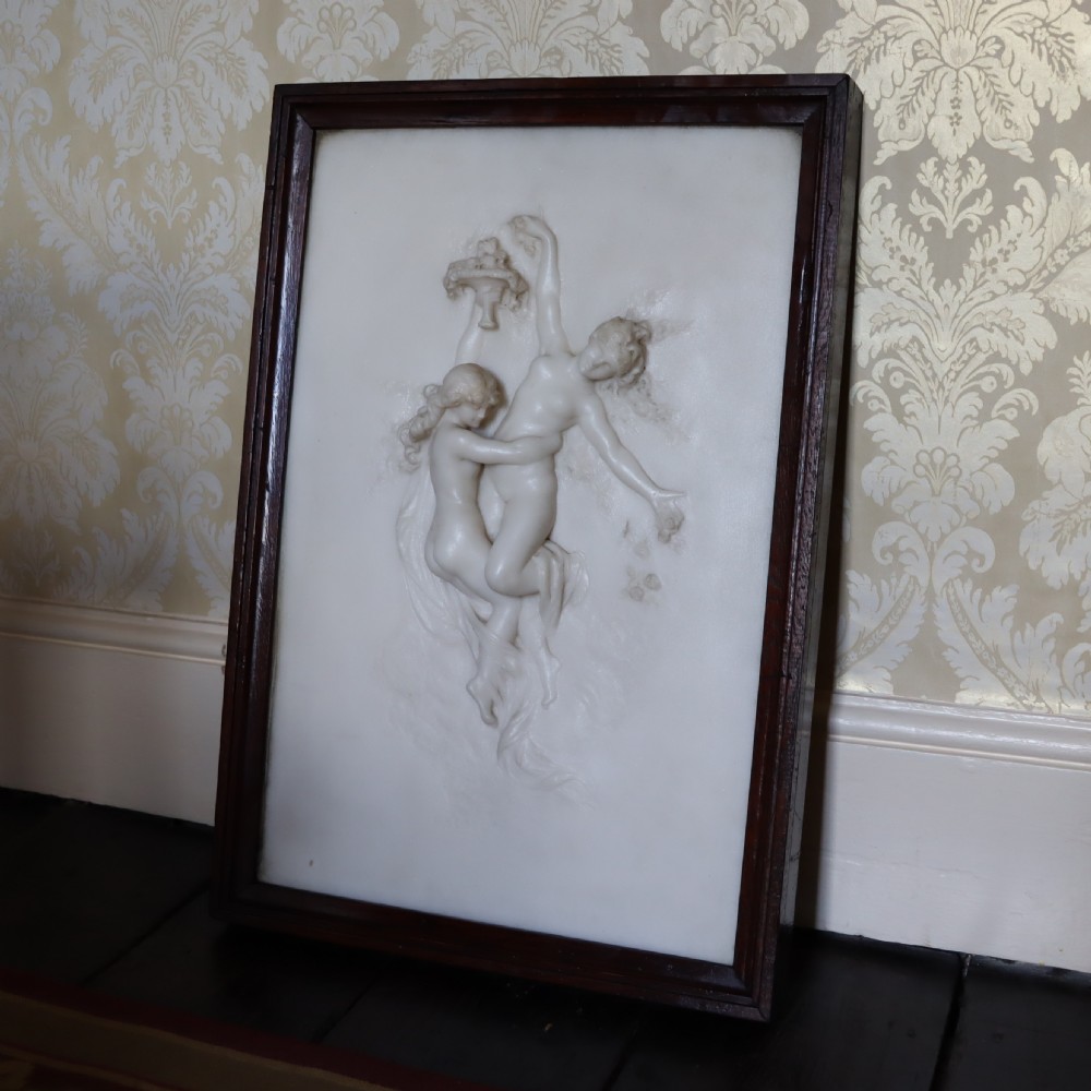 A rectangular dark wood frame enclosing a carved white marble relief sculpture depicting two classical figures in motion.