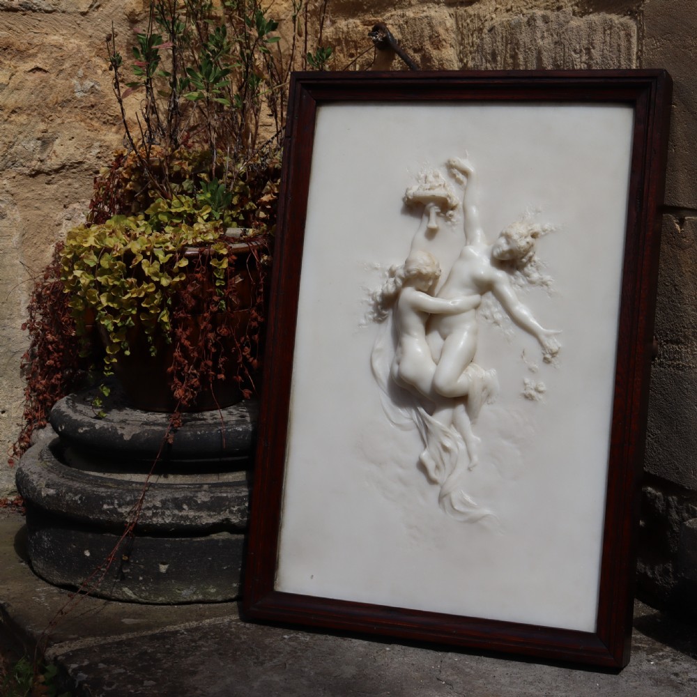 A rectangular dark wood frame enclosing a carved white marble relief sculpture depicting two classical figures in motion. View II