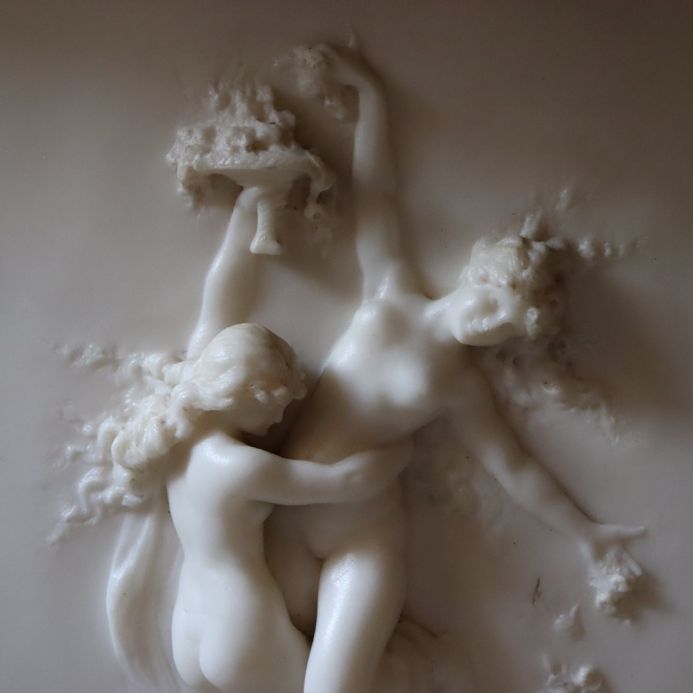A rectangular dark wood frame enclosing a carved white marble relief sculpture depicting two classical figures in motion. View III