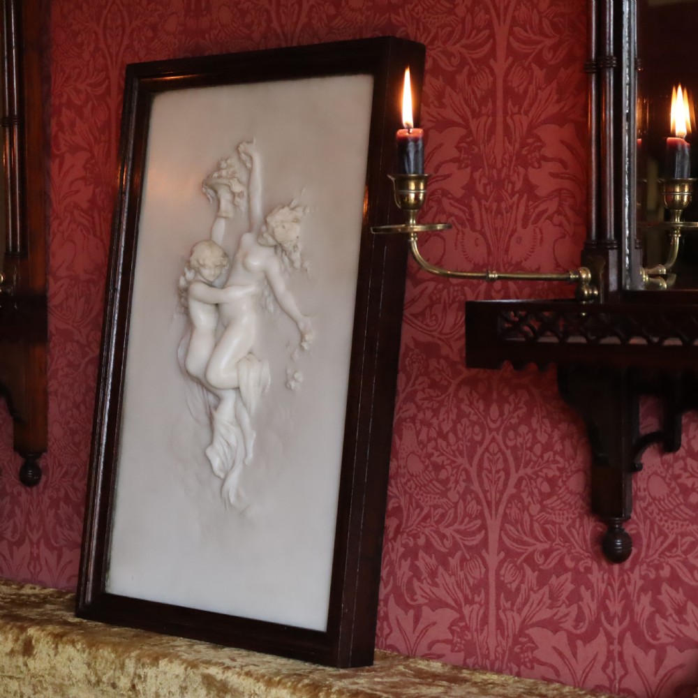 A rectangular dark wood frame enclosing a carved white marble relief sculpture depicting two classical figures in motion. View V