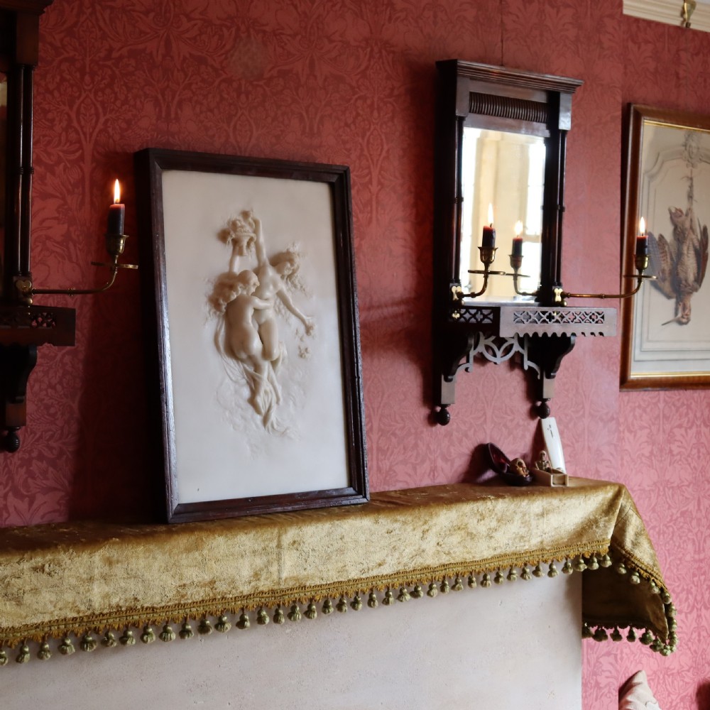 A rectangular dark wood frame enclosing a carved white marble relief sculpture depicting two classical figures in motion. View VI