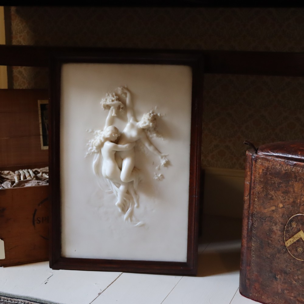A rectangular dark wood frame enclosing a carved white marble relief sculpture depicting two classical figures in motion. View VII